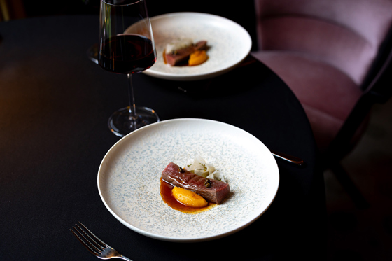 Two plates with small portions of steak with a glass of red wine between them.